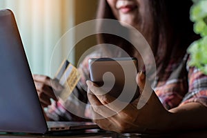 Woman hands holding credit card, using mobile smartphone for online shopping and payment with laptop computer