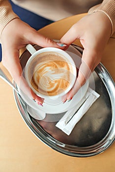 Woman hands holding cup of cappuccino, top view. Morning mood with coffee. Coffee shop