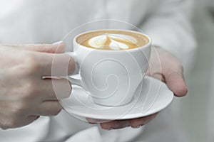 Woman hands holding cup of hot coffee latte cappuccino with with lush milk foam heart shaped.