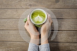Woman hands holding cup of hot green tea with heart shaped.