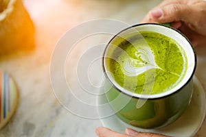 Woman hands holding cup of hot green tea with heart shaped.