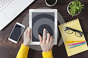 Woman hands holding digital tablet at wooden office desktop, top view