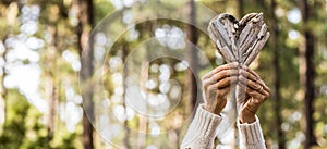 Woman hands holding firewood in shape of heart against trees in forest, woman showing heart shape made from bark. Female hands