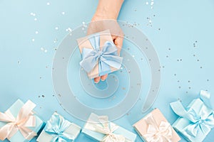 Woman hands holding gift or gift box decorated with confetti on blue pastel table top view. Flat composition for birthday or