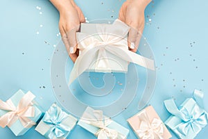 Woman hands holding gift or gift box decorated with confetti on blue pastel table top view. Flat composition for birthday or