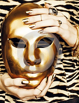 Woman hands holding golden carnival halloween mask, rich luxury manicure and jewelry close up on zebra print, fashion