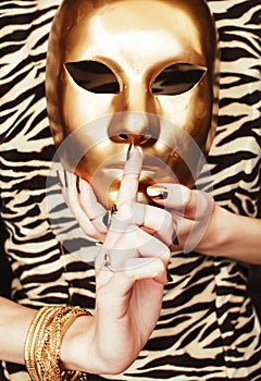 Woman hands holding golden carnival mask, rich luxury manicure and jewelry close up on zebra print, gold everythere