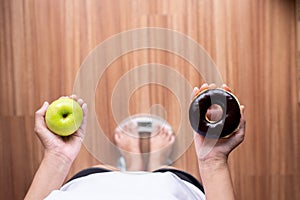 Woman hands holding green apple and baked chocolate donut during standing on weighing scale,Healthy diet,Dieting concept