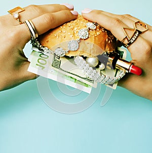 Woman hands holding hamburger with money, jewelry, cosmetic, social issue wealth concept close up