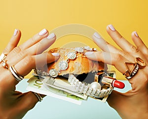Woman hands holding hamburger with money, jewelry, cosmetic, social issue wealth concept close up