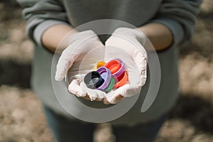 Woman hands are holding a handful of colorful plastic lids. Concept of environmental pollution, eco friendly behavior.