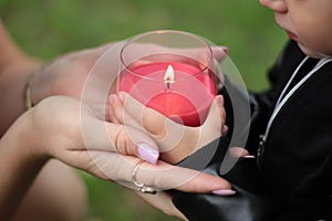 Red burning candle holding the hands of a child. Earth Hour. A child with a candle