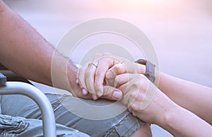 Woman hands holding her husband`s hand on wheelchair during rehabilitation for encouragement in outdoor area