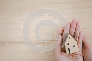 Woman hands holding home model with care on wooden background