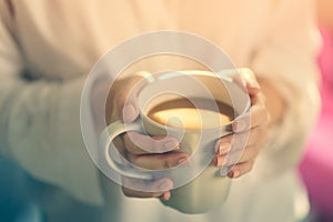Woman hands holding hot cup of coffee or tea in morning sunlight