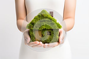 Woman hands holding little eco house made from green grass on white background