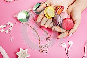 Woman hands holding macaroons with lot of girl stuff on pink background, girls accessories concept