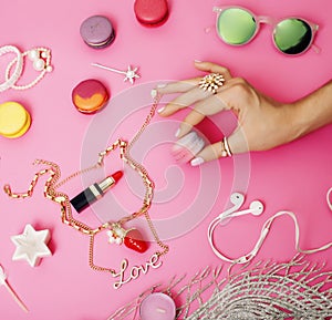 woman hands holding macaroons with lot of girl stuff on pink background, girls accessories concept close up