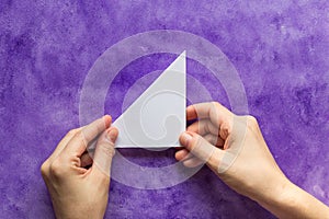 Woman hands holding made folded paper triangle on the violet surface
