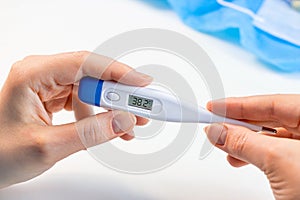 Woman hands holding a medicine digital thermometer with high body temperature measurement on light background. Fever, flu illness