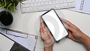 Woman hands holding mobile phone with empty screen on whote office desk.
