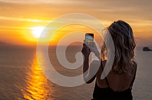 Woman hands holding mobile phone at sunset. Young curly hair woman taking photos with her cell phone in a beautiful