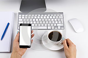 Woman hands holding the phone with screen and cup of coffee. Business workplace with keyboard and business objects