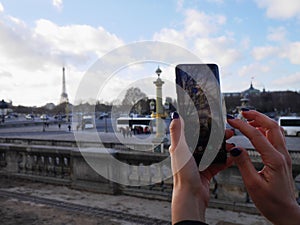 Woman  hands holding the phone and take a picture of the Eiffel tower.  in urban space