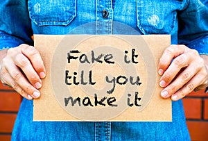 Woman hands holding piece of cardboard with phrase Fake It Till