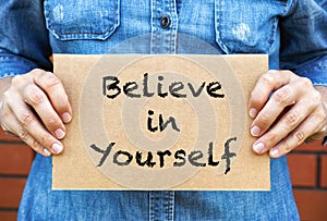 Woman hands holding a piece of a cardboard with words Believe in Yourself
