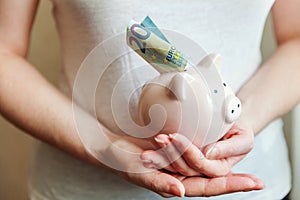 Woman hands holding pink piggy bank and putting money Euro
