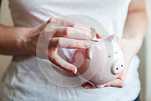 Woman hands holding pink piggy bank and putting money Euro coin