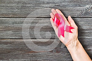 Woman hands holding pink ribbon on wooden background. Top view, with copy space for text. Breast cancer awareness.