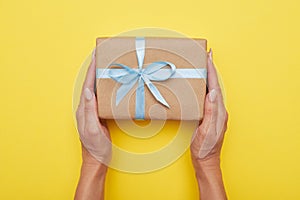 Woman hands holding present with box decorated with blue ribbon