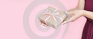 Woman hands holding present box with pinlk bow on pastel pink background