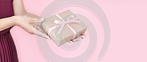 Woman hands holding present box with pinlk bow on pastel pink background