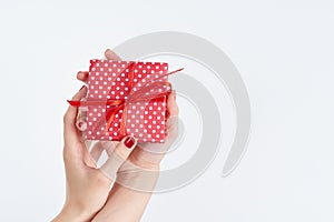 Woman hands holding red gift with ribbon, manicured hands with nail polish on white background with copy space