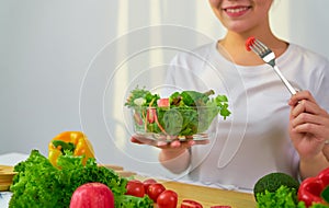 Woman hands holding salad bowl with eating tomato and various green leafy vegetables on the table at the home.