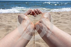 Woman hands holding sand heart against seaside background. Seaside and sand heart in hands. Vacation and relax concept.
