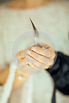 Woman hands holding single feather in her hands, light pastel colors