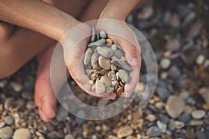 Woman hands holding small stones in hands on beach background with burning sun