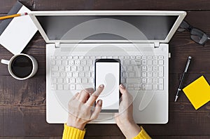 Woman hands holding smartphone at wooden office desktop, top view