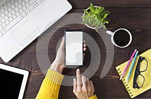 Woman hands holding smartphone at wooden office desktop, top view