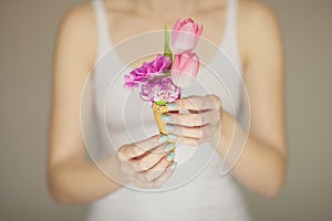 Woman hands holding spring flowers in an ice cream cone, sensual studio shot