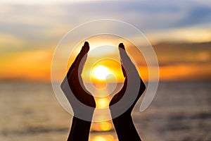 Woman hands holding the sun during sunrise or sunset.