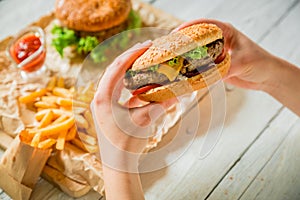 Woman hands holding tasty american burger and french fries, sauce on wooden plate