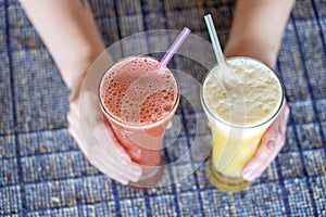 Woman hands holding two glasses with pineapple and watermelon fresh juice, close up