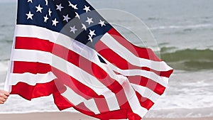 Woman hands holding USA flag in the beach on the background of sea waves