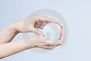 Woman hands holding waterproof silicone facial cleansing brush on light blue background. Modern brush for face cleansing
