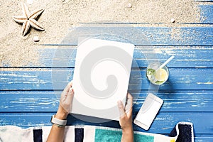 Woman hands holding white blank magazine cover mockup on beach towel